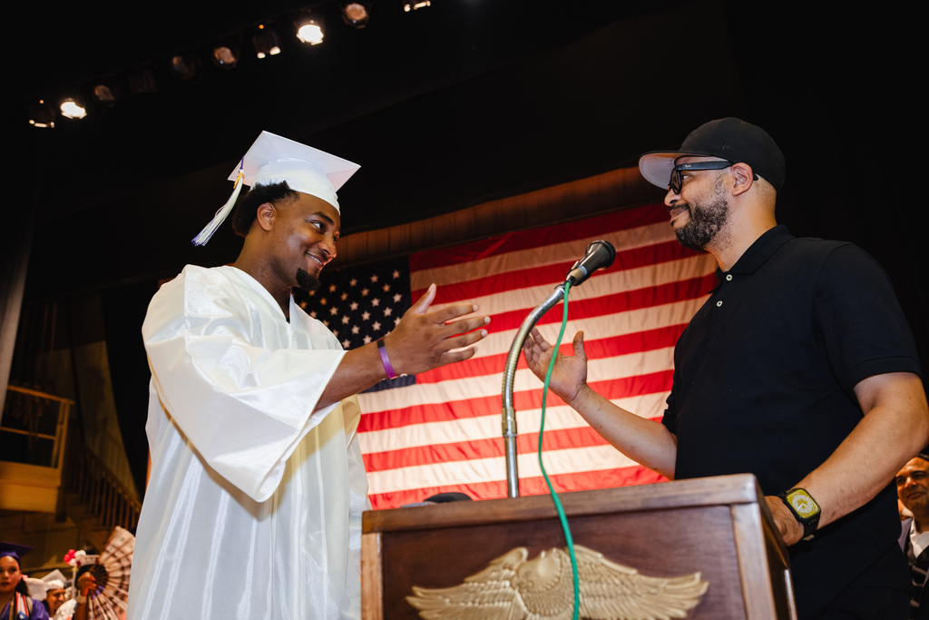Graduate goes to great teacher and shake hands on stage as he walks towards him.