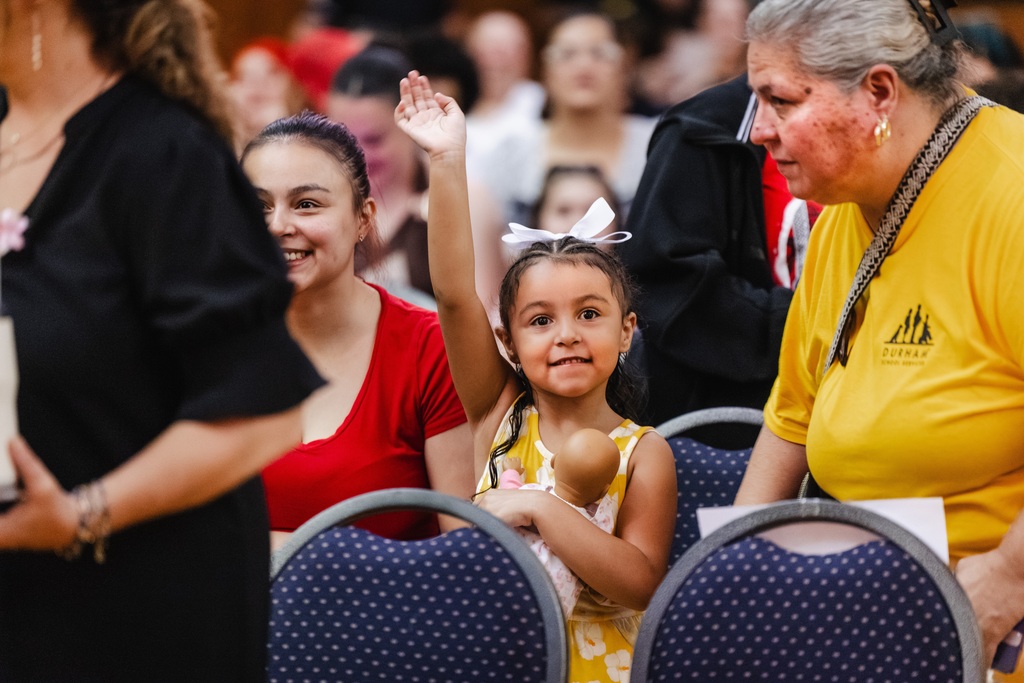 Young girl with her doll waves from the audience.