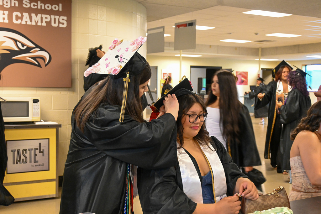 One graduate fixes the others cap in the cafeteria before graduation.
