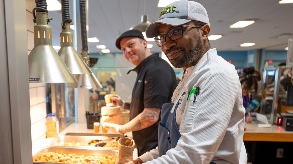 Chef Green and HPS staffer turn and smile at the camera while cooking