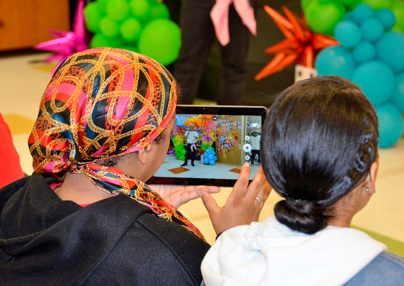 Woman with head scarf viewing student event through photo app on tablet