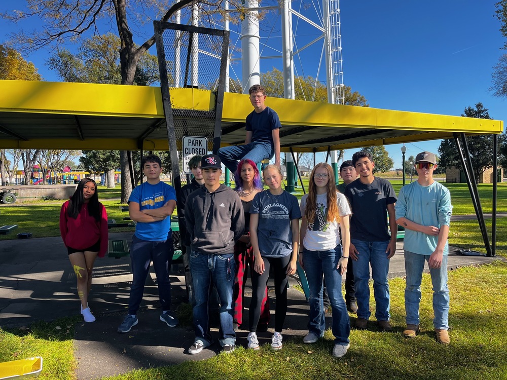 Group of student pose in front of a yellow pavilion they just painted