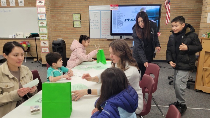 A teacher leads a group of students and their parents in a math card game at at table.