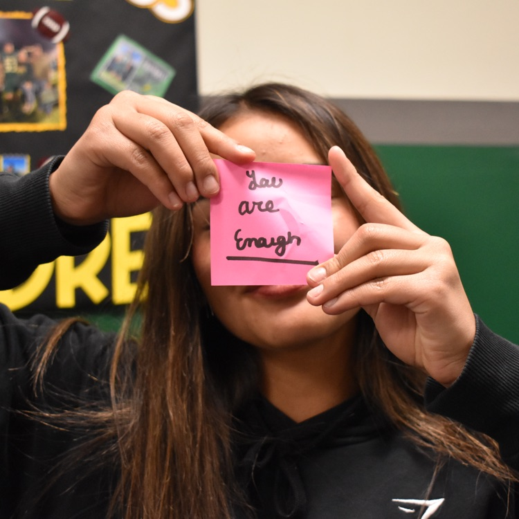 Girl holds up sticky note that reads "You are enough" 