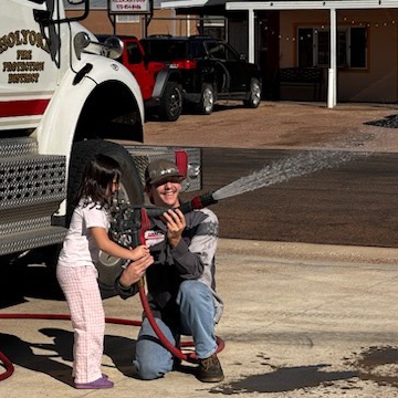 firefighter holds hose with little girl