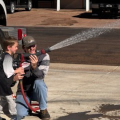 firefighter holds hose with little boy