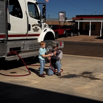 firefighter holds hose with little boy
