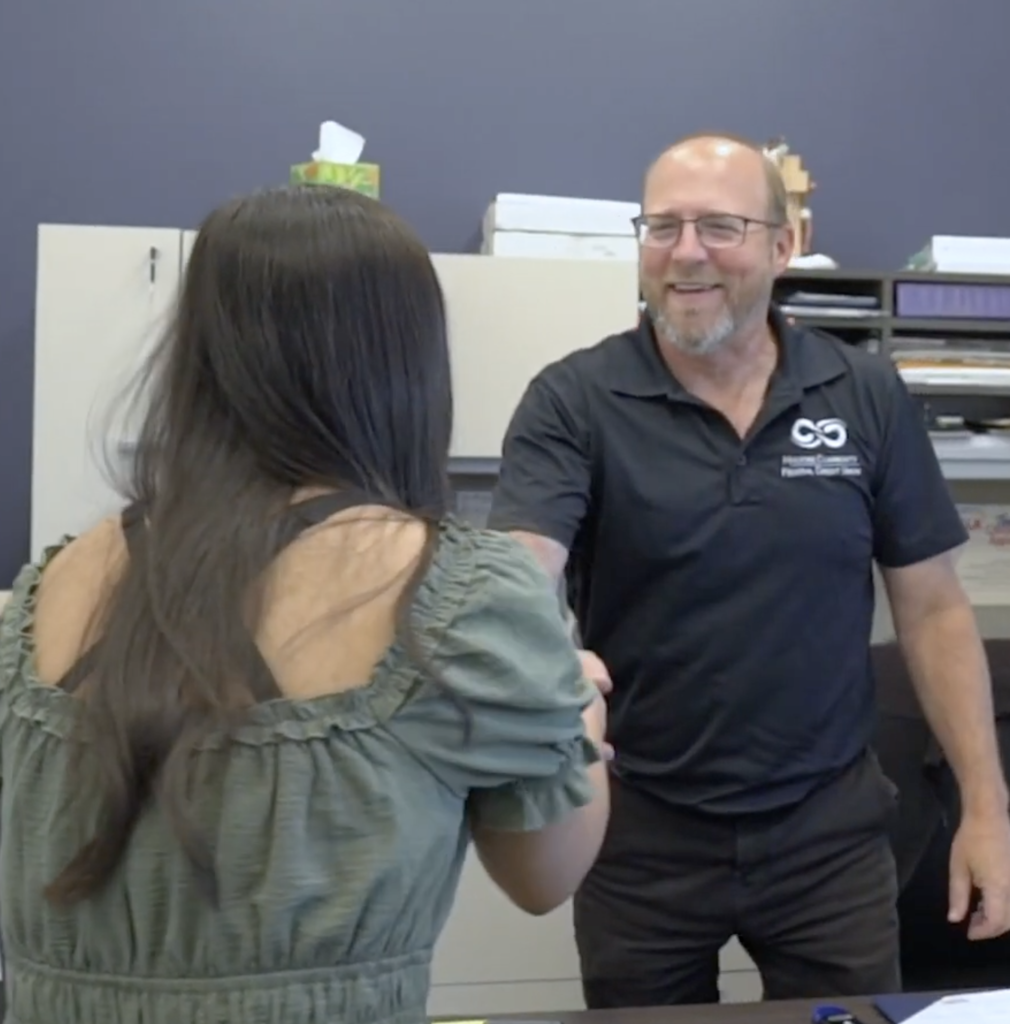 Two people smiling and shaking hands in an office.
