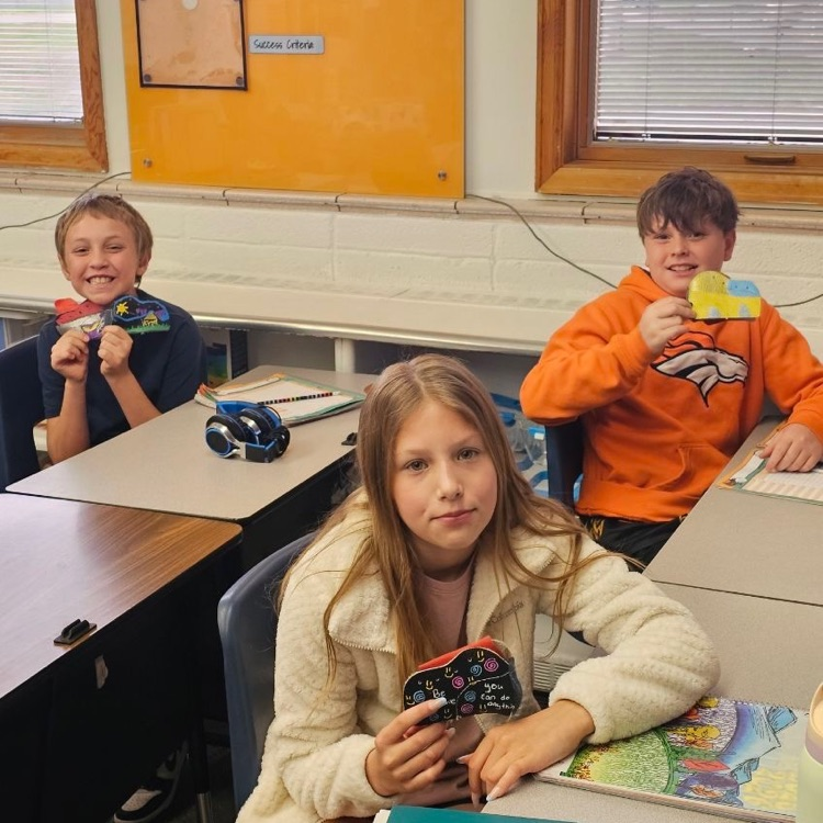 Students smile while holding up projects 