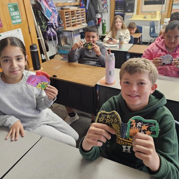 Students smile while holding up projects 