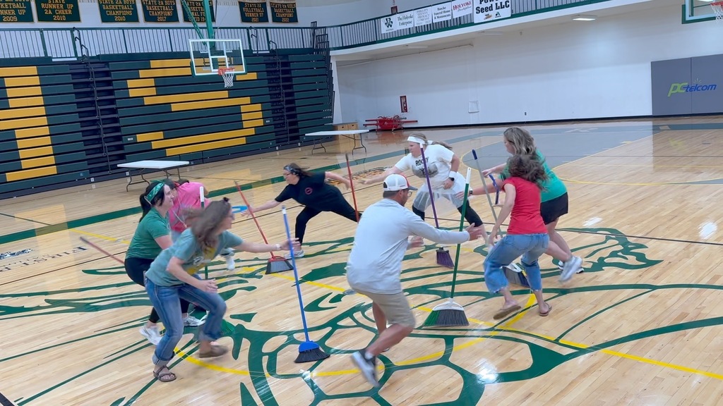 a group of people stand in a circle. they are racing to try and grab a broom before it falls to the ground.