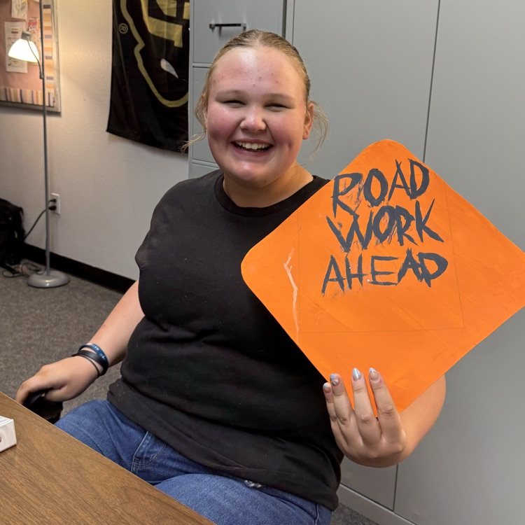 student poses with a road work sign