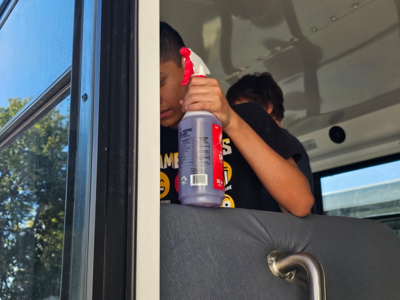student washing the inside of the windows on the school mini bus