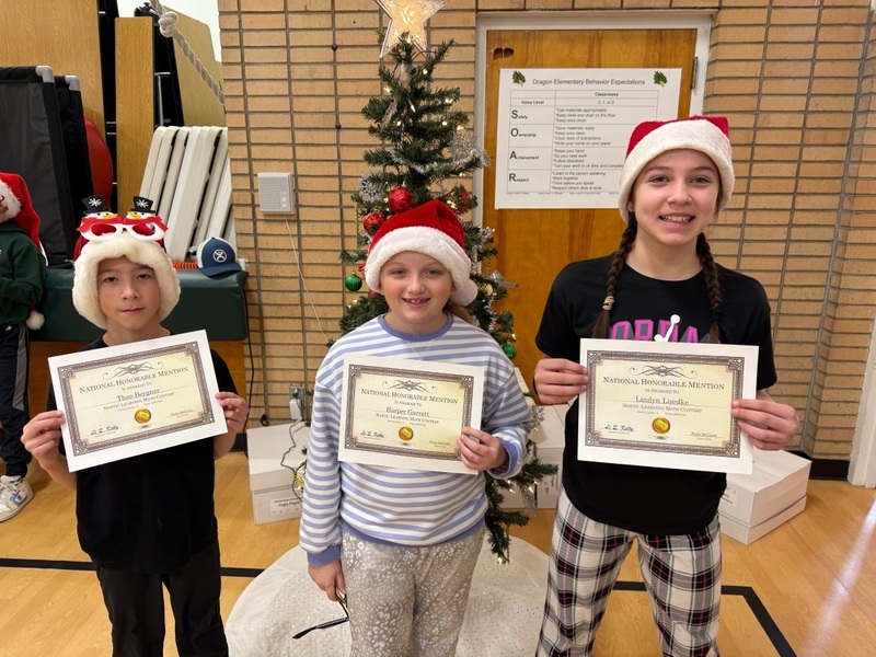 students in pajamas and Santa hats holding certificates standing in front of a Christmas tree