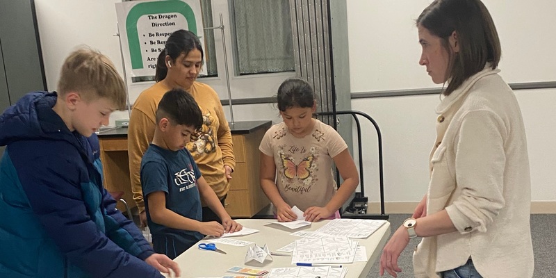 a teacher looks on while three students and a parent make cootie-cachers
