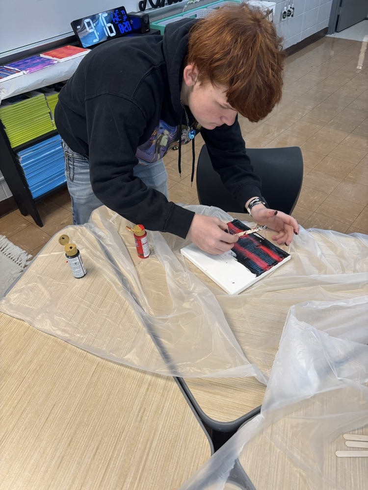 male student using popsicle stick to paint canvas 