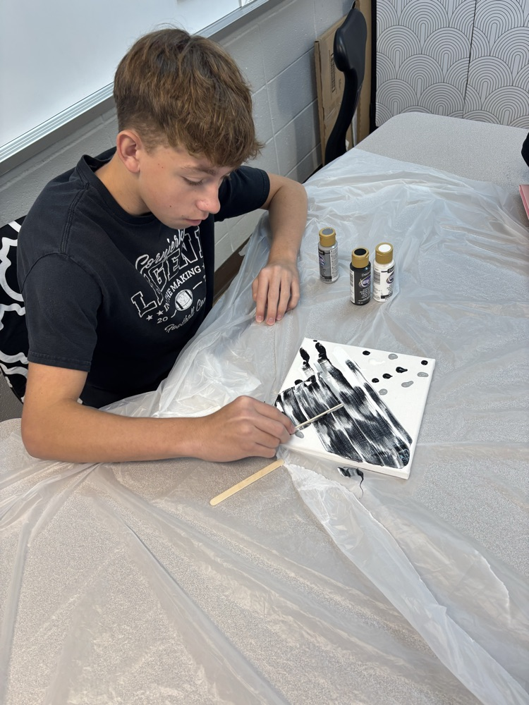 male student using popsicle stick to paint canvas