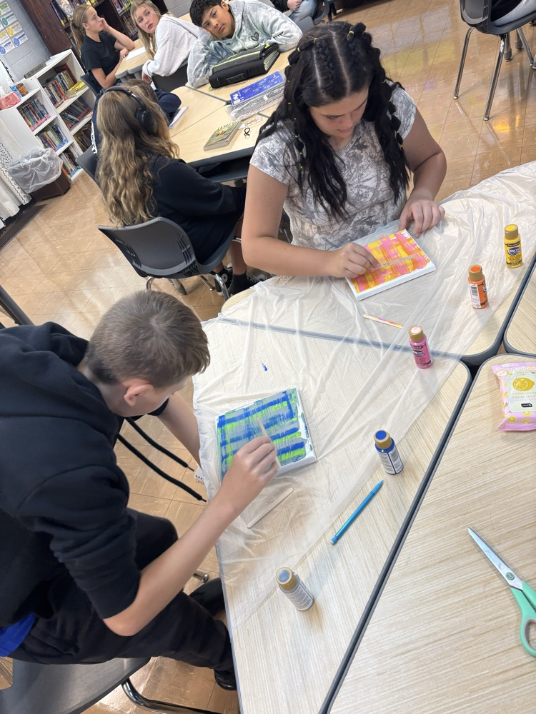male and female students using popsicle stick to paint canvas