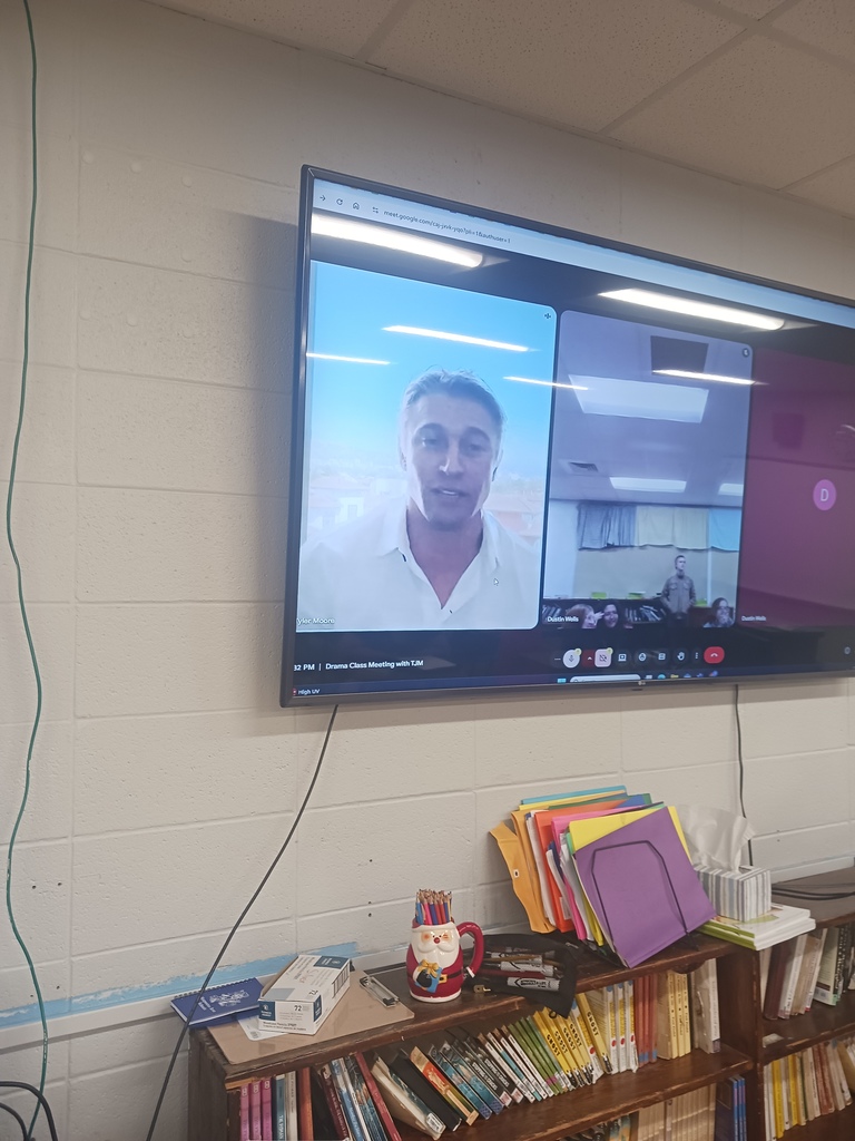 Screen on the classroom wall with Tyler Jacob Moore appearing before the class in a Google Meet.