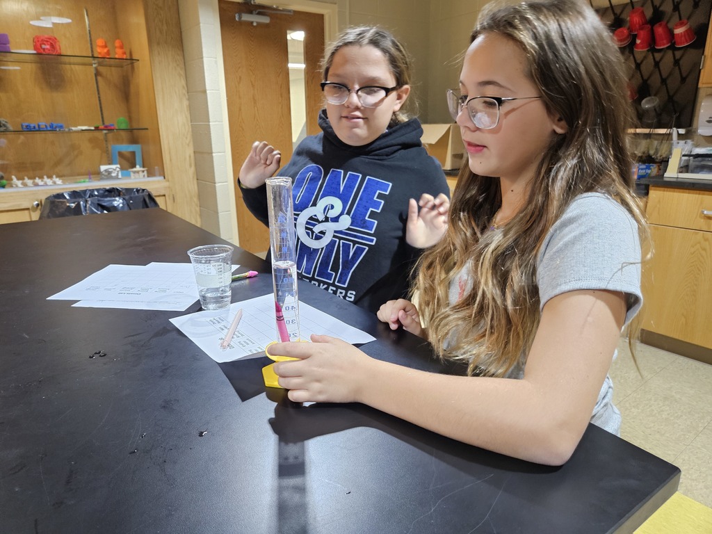Students measure the amount water moved in a graduated cylinder when adding a pink crayon. 