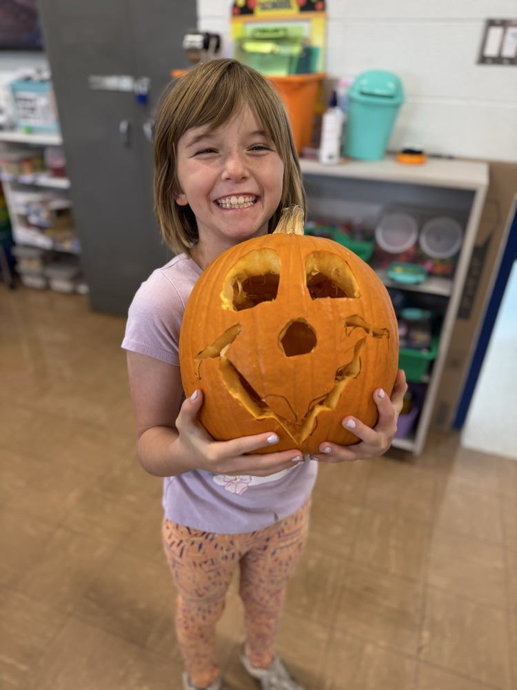 student holding a carved pumpkin inside a classroom