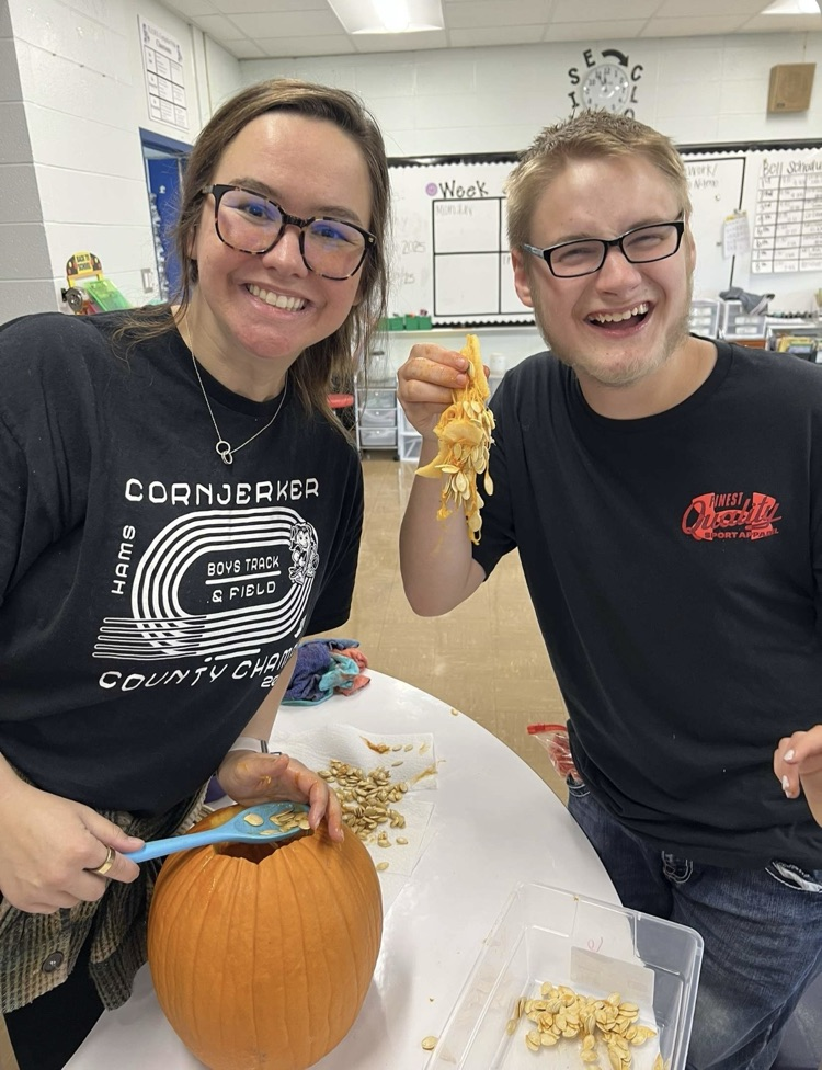 teacher and student smiling while scooping seeds out of a pumpkin