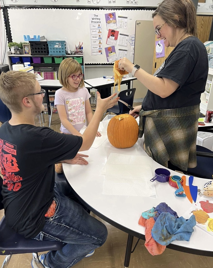 students looking at the insides of a pumpkin while a teacher holds it