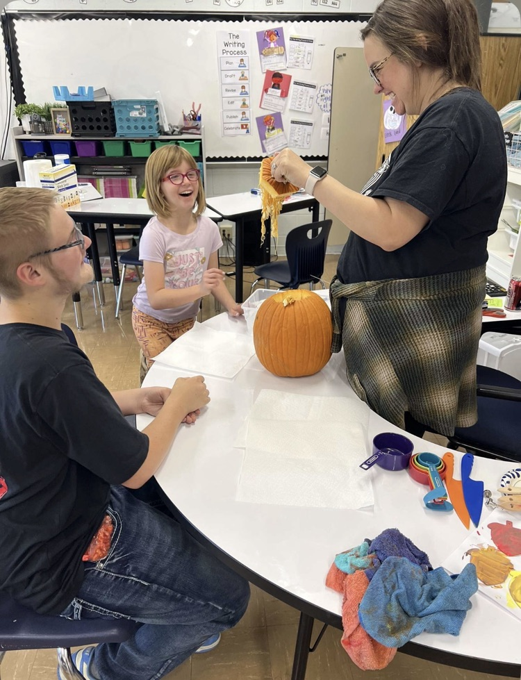 students smiling and looking at the insides of a pumpkin while a teacher holds it.