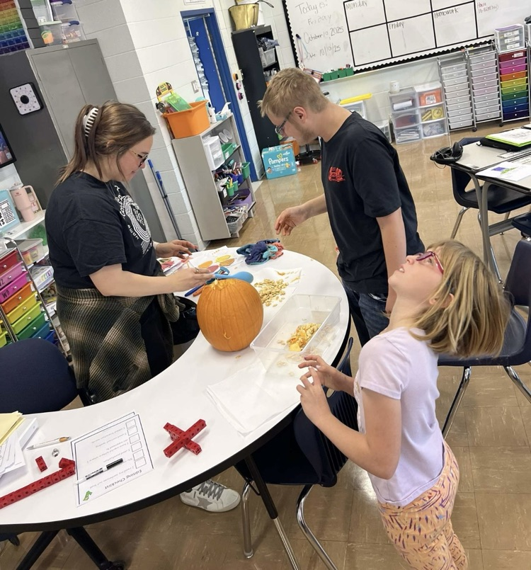students and teacher gathered around a table gutting a pumpkin