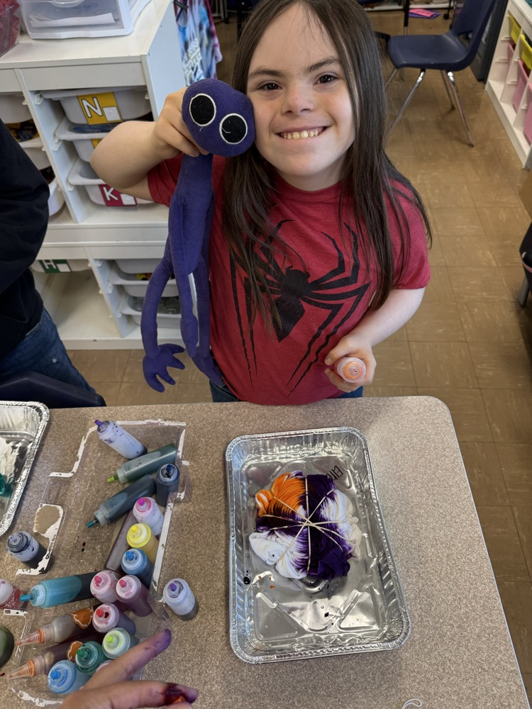 student with Down syndrome holding a doll while tie dying a tshirt 