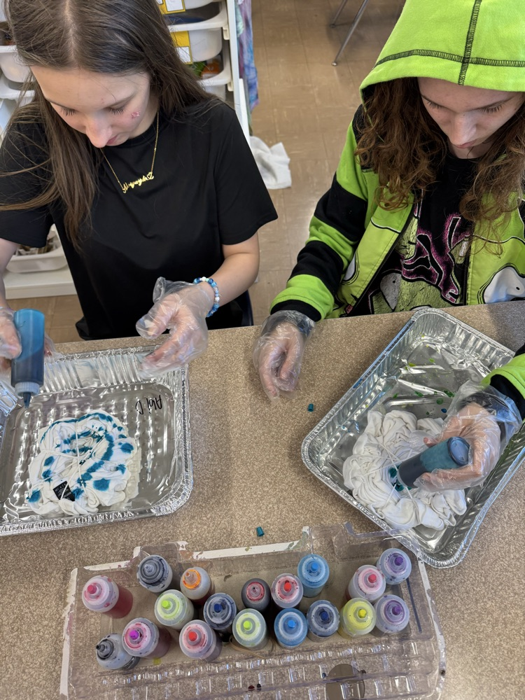 two students working on tie dye together while smiling 