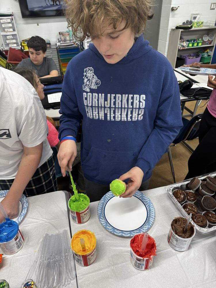 one male student in a cornjerker sweatshirt icing a cupcake