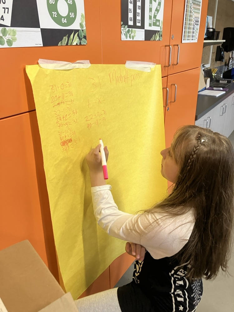students working out math problems on a large paper on the wall