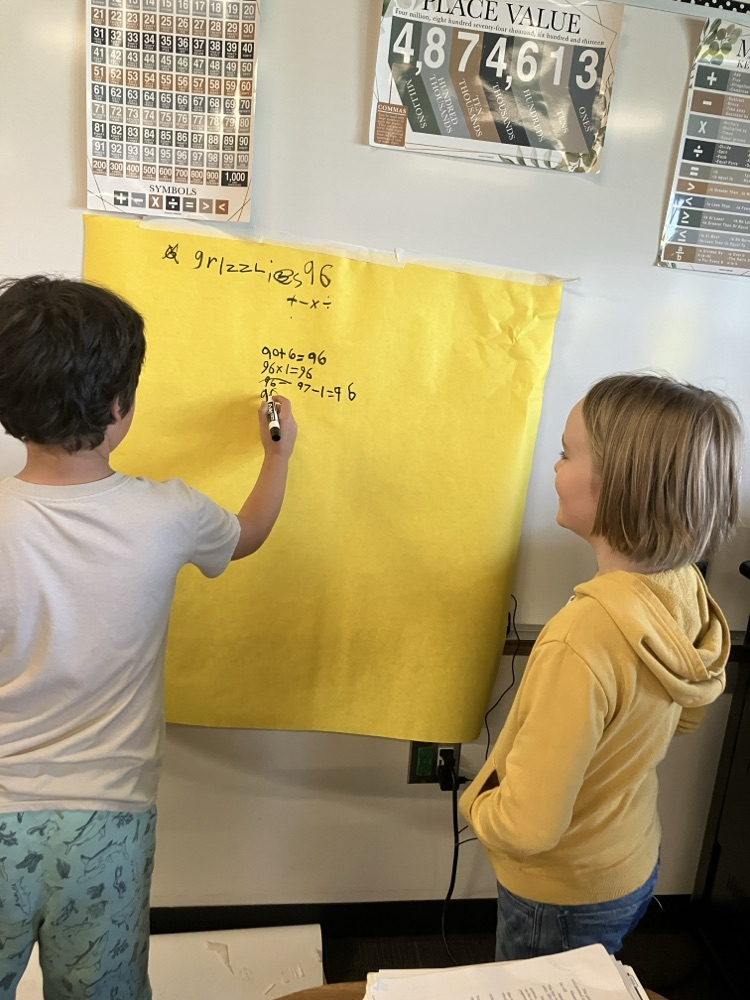 students working out math problems on a large paper on the wall
