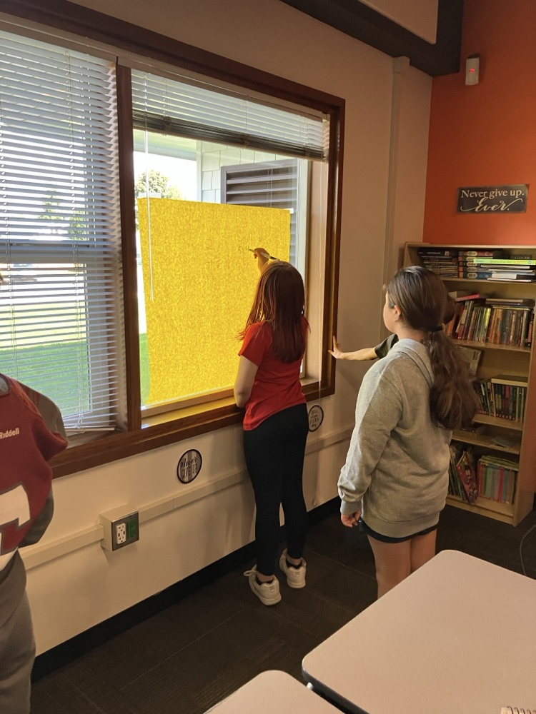students working out math problems on a large paper on the wall