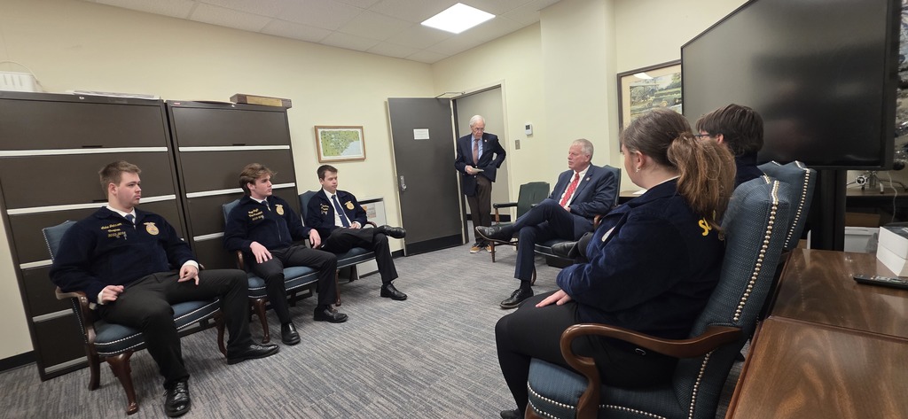 A meeting in a conference room with participants in uniforms and one person standing.