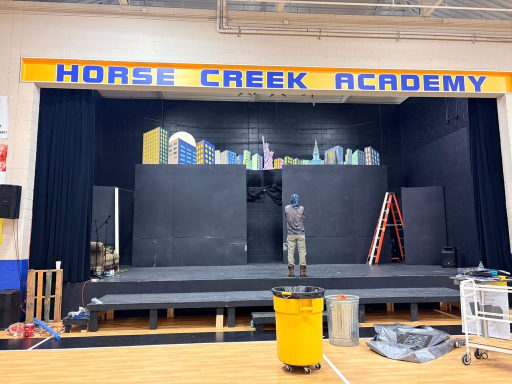 A stage at Horse Creek Academy with a person working on it. A yellow trash bin is on the floor.