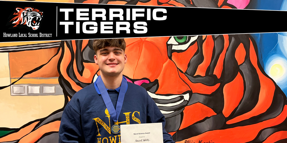 student standing in front of tiger mural with award