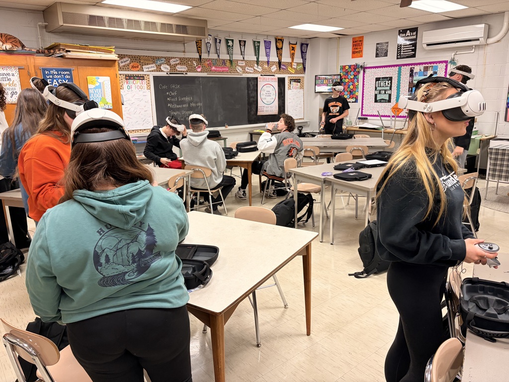 Students wearing virtual reality headsets and participating in simulated culinary or workplace environments in a classroom setting.