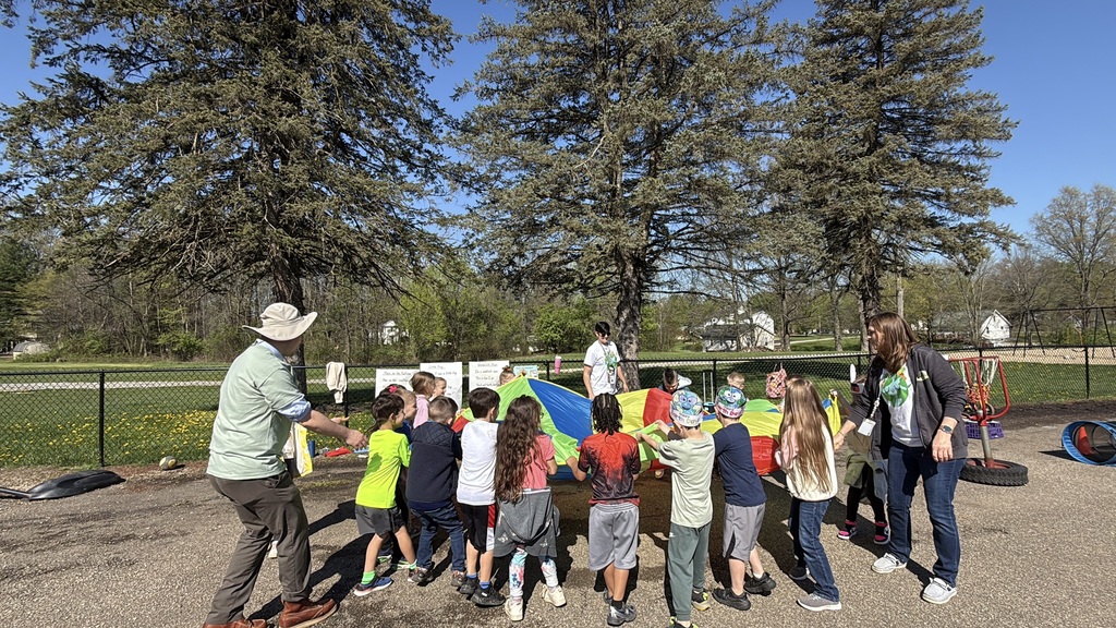 Students celebrating Earth Day outside, touring the Tiger Den, making bird seed, drawing with chalk, painting rocks, and playing with parachutes.