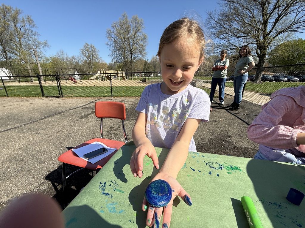 Students celebrating Earth Day outside, touring the Tiger Den, making bird seed, drawing with chalk, painting rocks, and playing with parachutes.