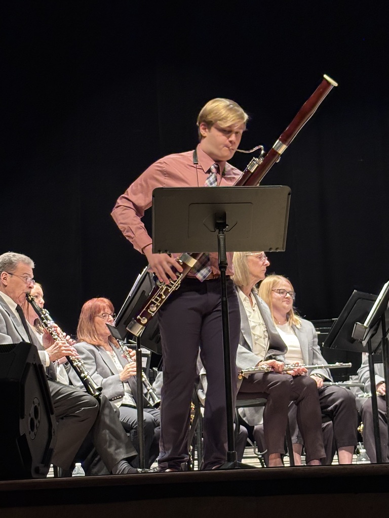 A student bassoonist performs as a soloist in front of a seated concert band during a live performance.