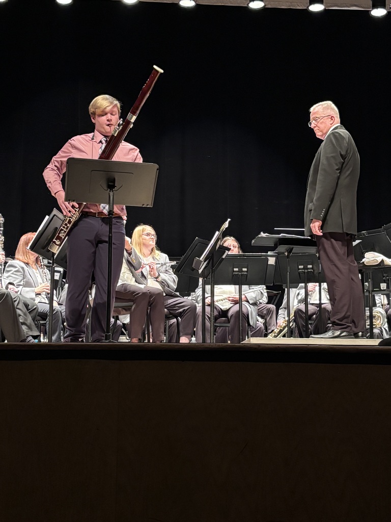 A student bassoonist performs as a soloist in front of a seated concert band during a live performance.