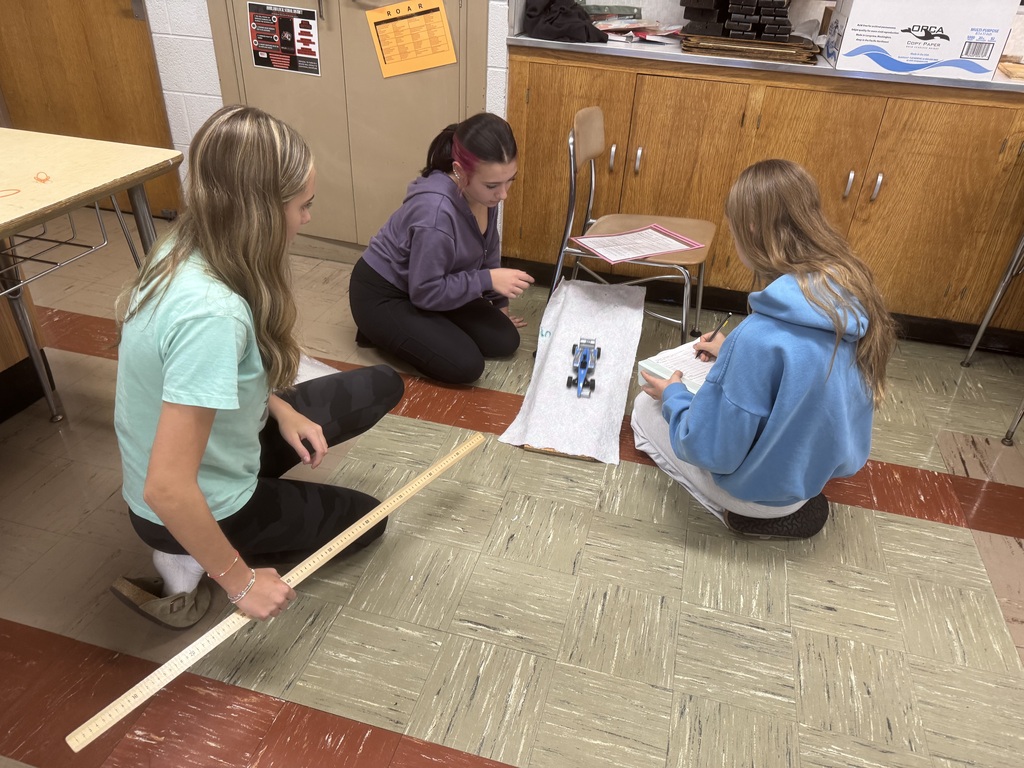 Howland Junior High School seventh-grade students display element cubes, while eighth-grade students investigate friction by testing toy cars on different surfaces and graphing their results.