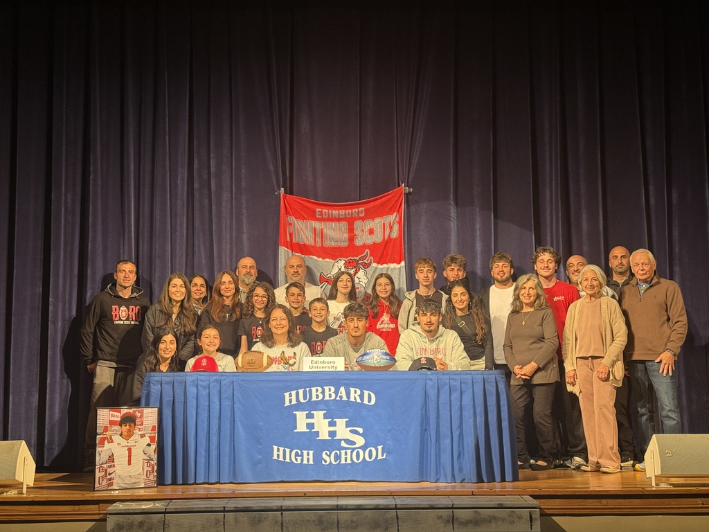 Michael Hazimihalis: Student-athlete seated at a table signing a letter of intent for football at Edinboro, with family and school representatives standing behind him.