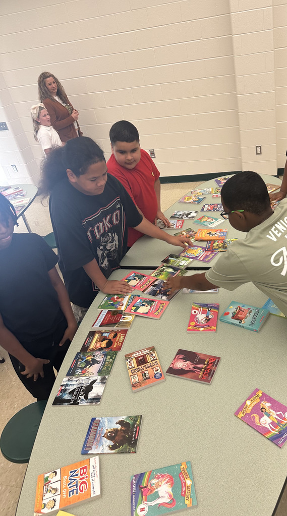 A group of students stands around a long cafeteria table covered with chapter books.