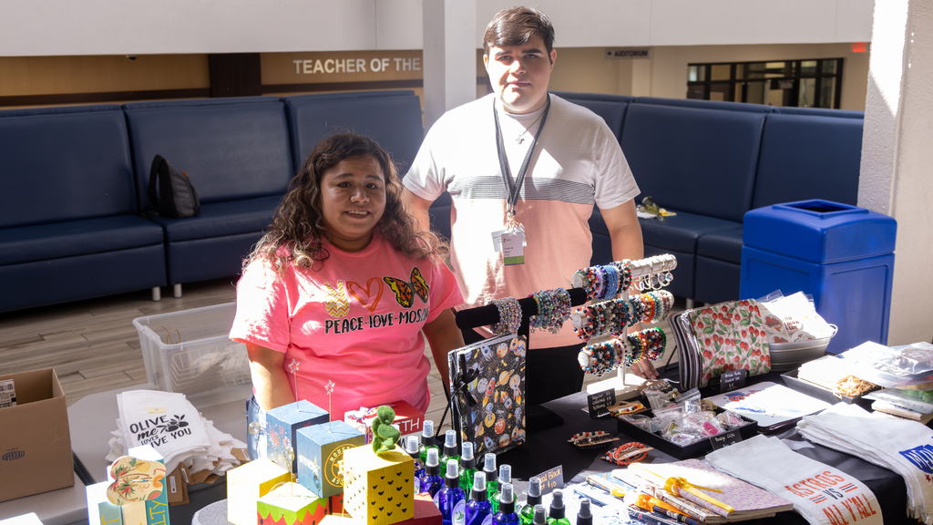 Students smiling behind a desk with merchandise