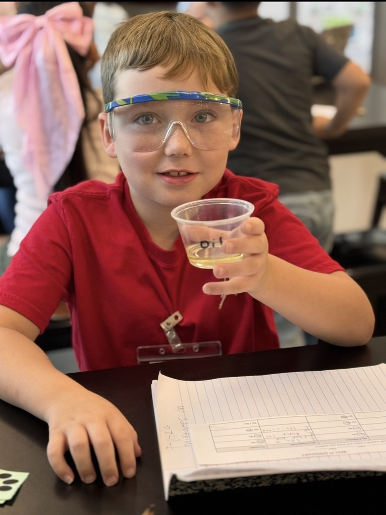 Student holding a cup of oil. Adding it to a beaker filled with water and test if it will or will not dissolve in water.