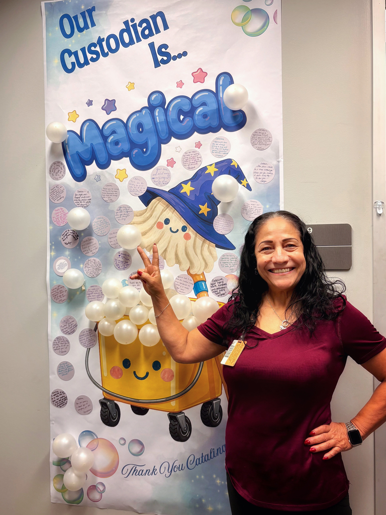Woman Smiling holding up a peace sign in front of a poster that reads "Our Custodian is Magical" and there's a wizard hat on a smiling mop and a yellow smiling bucket with bubbles floating around created by balloons.