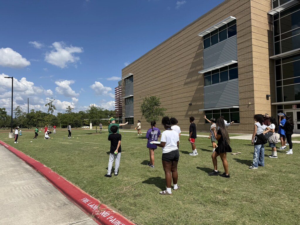 Many people in a grassy field in front of a large building with glass windows.
